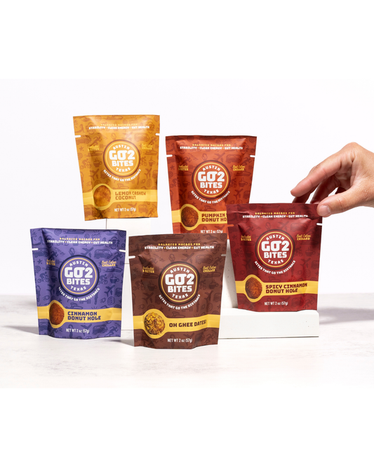 Five packages of GO2 Bites on a white background with a hand reaching for one package.